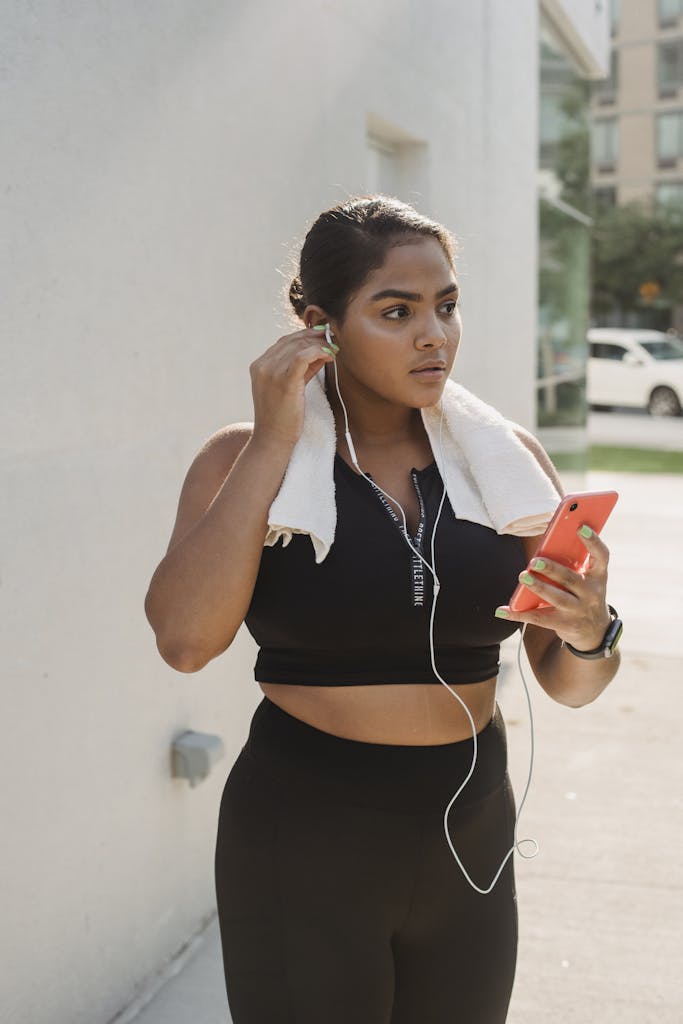 A Woman in Black Clothes Holding Her Mobile Phone while Wearing Earphones on Her Ear